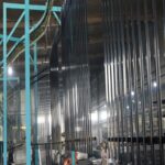 Bulk stacked black powder coated sword top palisade fence panels inside factory workshop for wholesale residential security supply | ANJIA