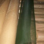 Stacked bulk dark green enamelled iron window screen rolls stored in factory warehouse for wholesale export supply | ANJIA