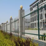 White and green powder coated steel palisade fence with spherical post caps, installed around office building landscape perimeter | ANJIA